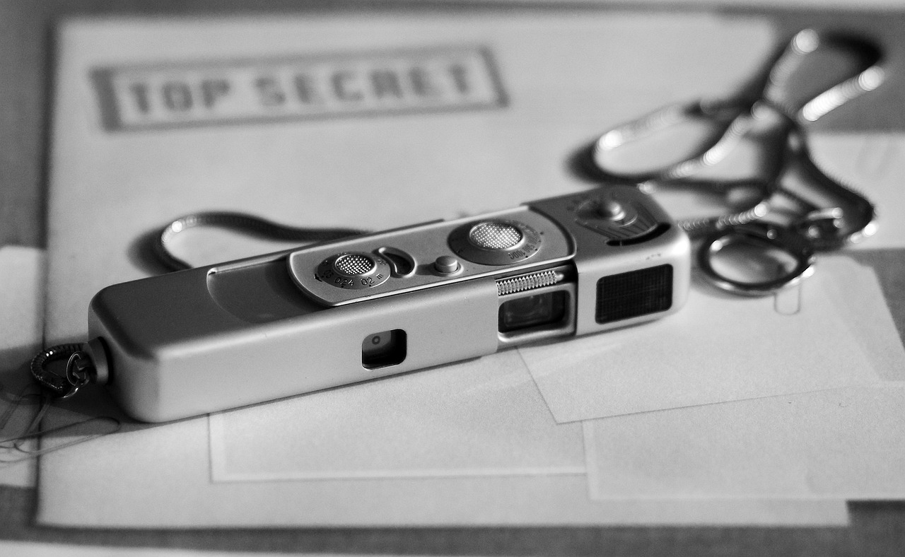Das Bild zeigt eine kleine Taschenkamera wie sie von Spionen genutzt werden und diese liegt auf einem Briefumschlag, der mit der Aufschrift Top Secret versehen ist.